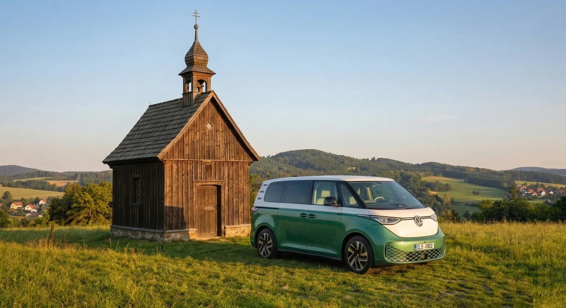 Green VW ID. Buzz parked by a wooden chapel on a hillside with rolling countryside
